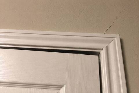 Gap between an interior door and its frame, with a crack running from the frame corner into the wall